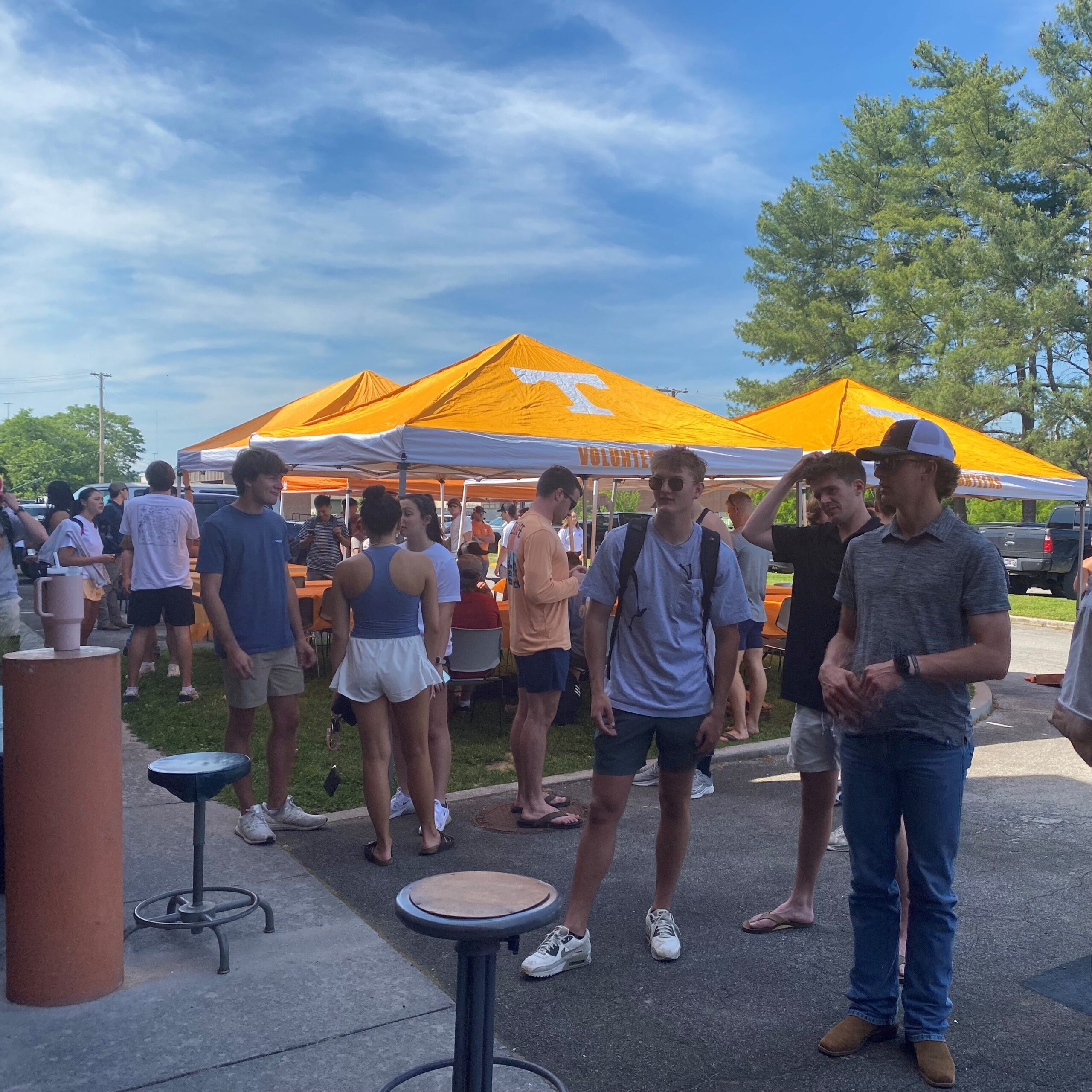 Group of students mingle at an outdoor event with University of Tennessee tents. 