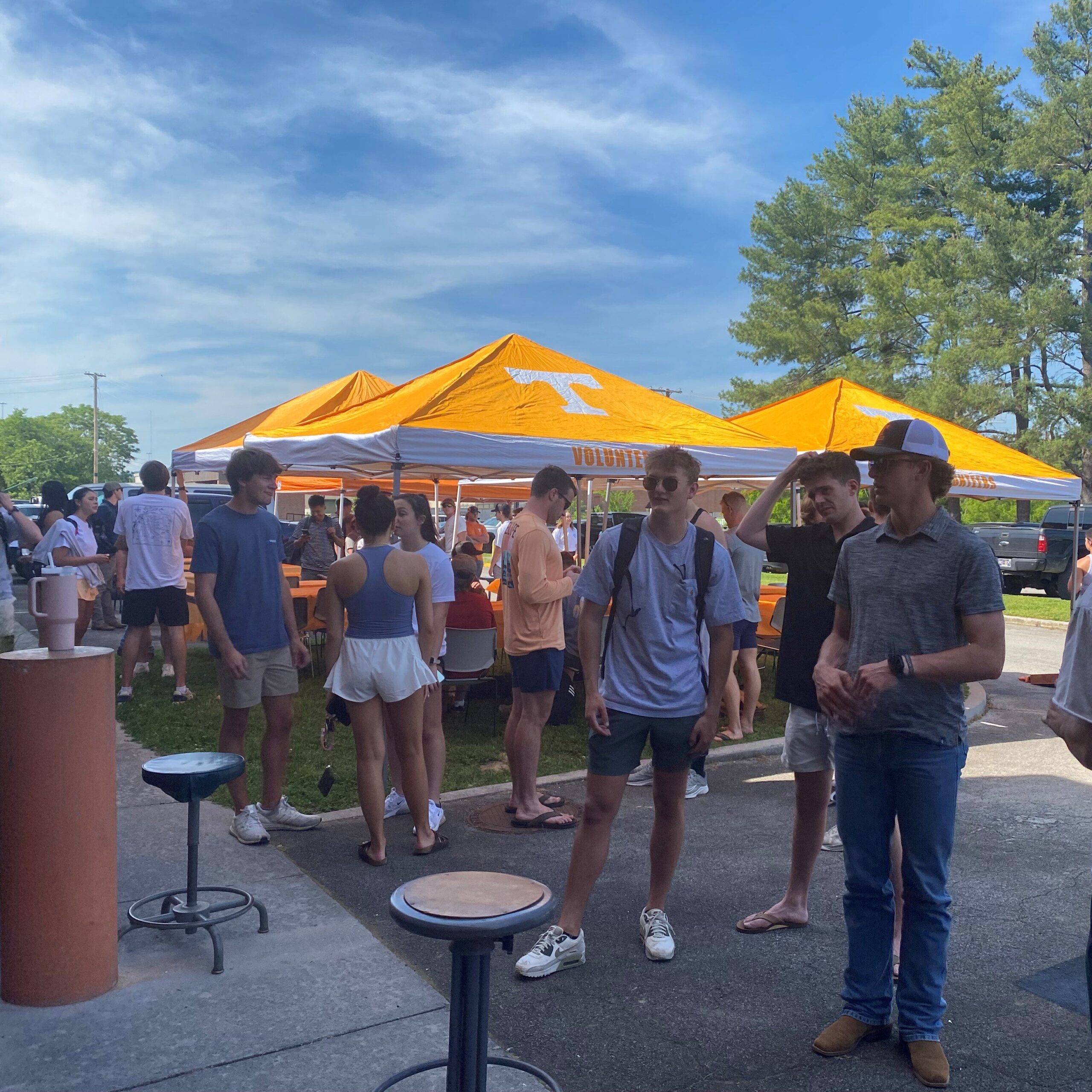 Group of students mingle at an outdoor event with University of Tennessee tents. 