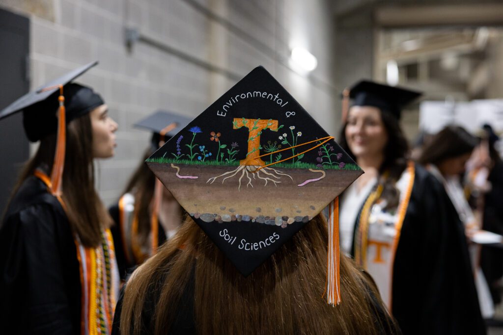 A student's graduation cap painted with the Power T in a garden that says "Environmental & Soil Sciences"